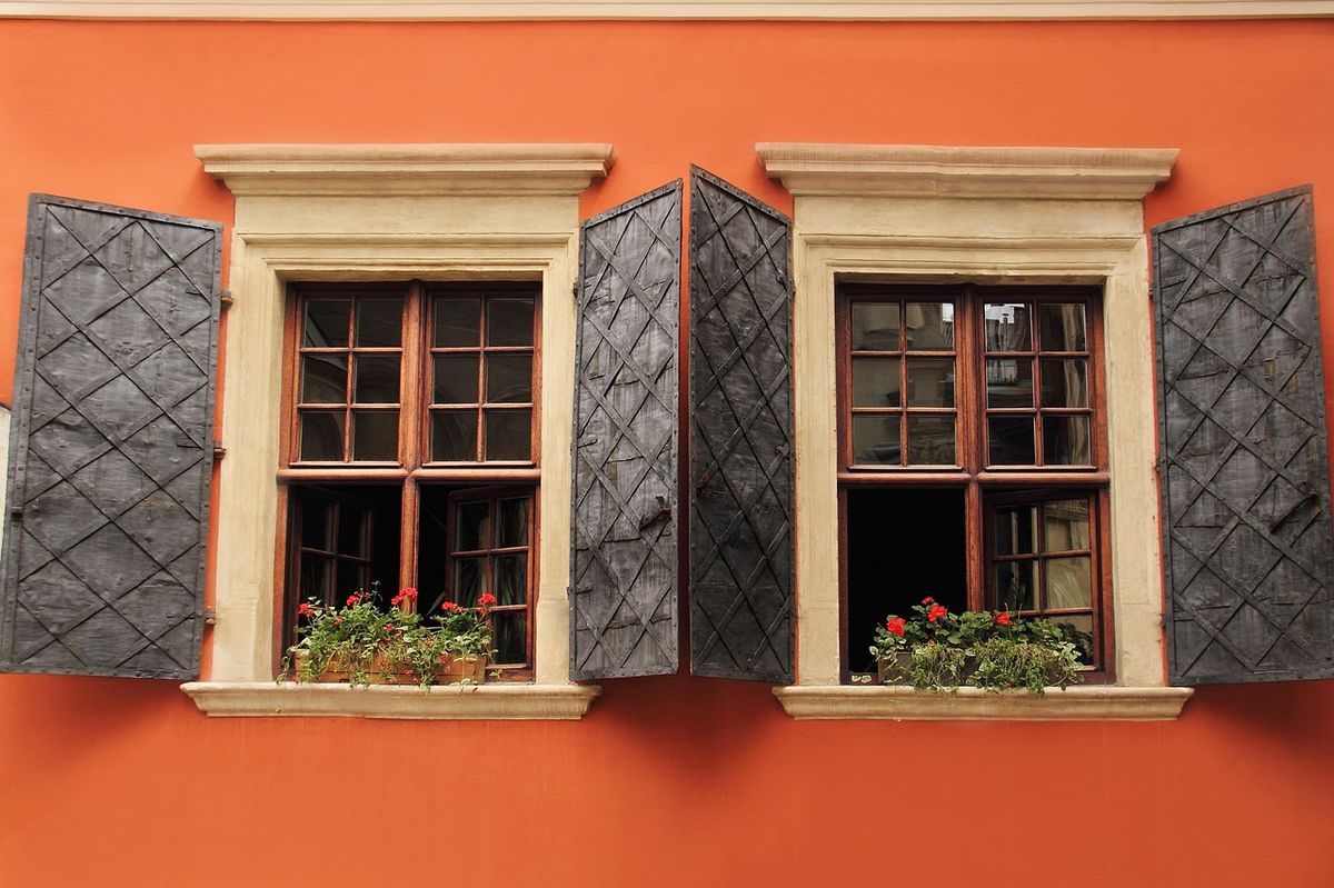 Fenêtres à volets avec jardinières de géraniums sur une façade colorée